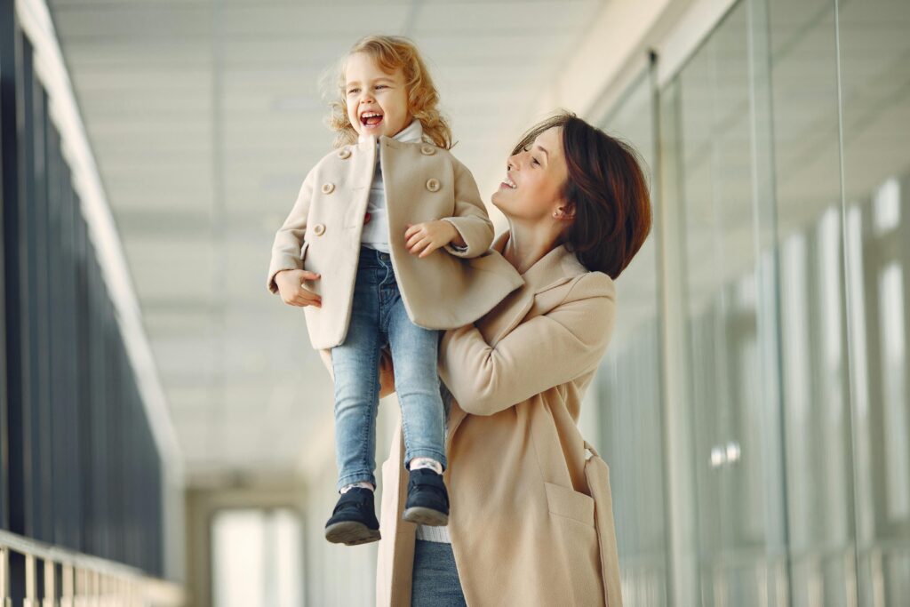 Mythe du parent parfait : 5 conseils pour une parentalité sereine A cheerful mother lifts her joyful young daughter. Capturing a moment of happiness and bonding indoors.